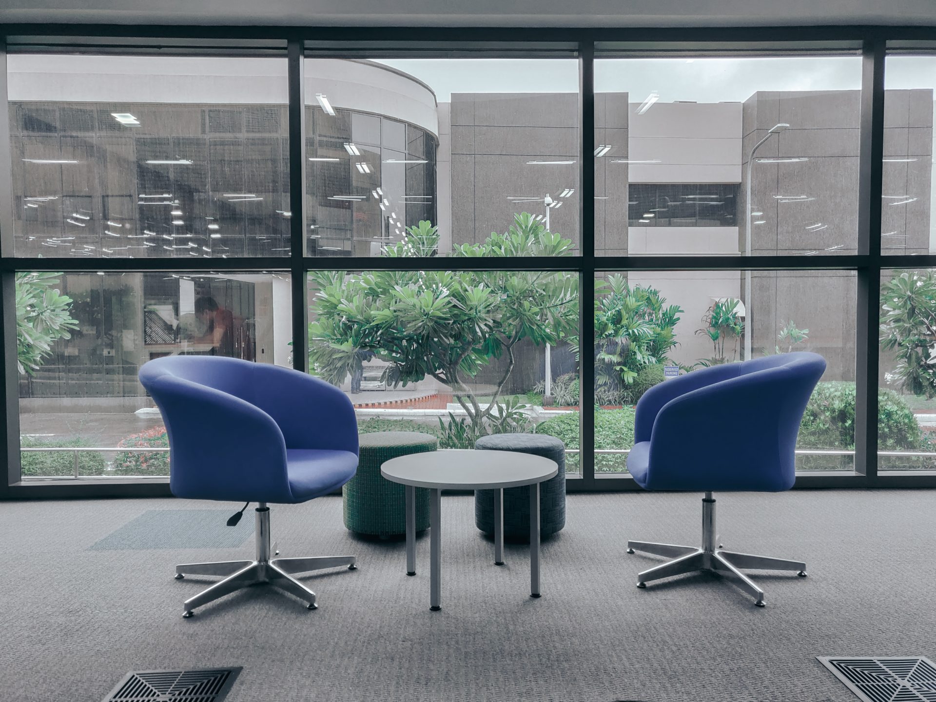 2 fauteuils bleus autour d'une table basse, devant une baie vitrée donnant sur les espaces verts d'une entreprise